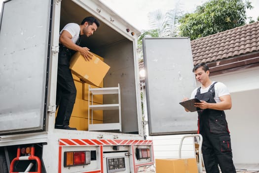 Uniformed removal company workers unload boxes and furniture from the truck exhibiting excellent teamwork. Their dedication guarantees a smooth move into the new home ensuring happiness. Moving Day