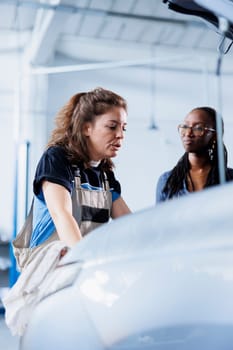 Hardworking mechanic at auto repair shop conducts annual vehicle checkup, informing client about needed engine replacement. Garage expert talks with customer after finishing car inspection