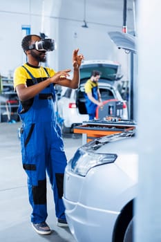 Specialist in auto repair shop using virtual reality to visualize car lights system in order to fix it. Knowledgeable garage worker wearing futuristic vr headset while repairing faulty vehicle