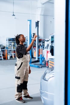 Trained mechanic in repair shop using holographic augmented reality to visualize car parts in order to fix them. BIPOC woman using AR technology while working on defective vehicle battery