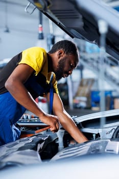 Engineer expertly examines car battery using advanced mechanical tools, ensuring optimal automotive performance and safety. BIPOC garage employee conducts annual vehicle checkup