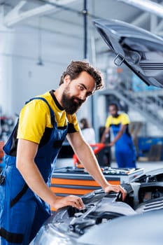 Portrait of car service mechanic examining broken engine using advanced mechanical tools to ensure optimal automotive performance and safety. Happy garage employee conducts annual vehicle checkup