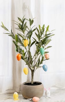 Easter marble decorative eggs hang on the branches of a green tree in a pot that stands on the sill of a window in the living room early in the morning, close-up side view.