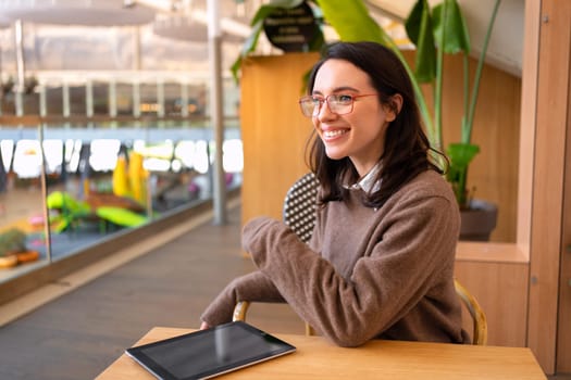 Woman with tablet computer sitting at her desk smile and looking side. Female freelancer person studying or working online on touch pad. Modern technologies and communication.