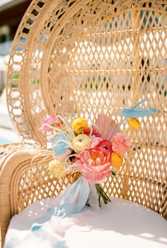 Bright bridal bouquet stands on a white cushion of a wicker armchair. High quality photo