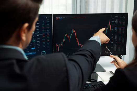 Two business traders discussing on dynamic stock market in currency rate investment trading on two pc screens with compare real time graph on risk or profit point of data at modern office. Postulate.