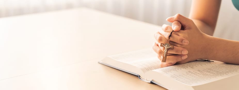 Cropped image of female reading a bible book while holding cross at wooden table with blurring background. Concept of hope, religion, faith, christianity and god blessing. Warm. Burgeoning.