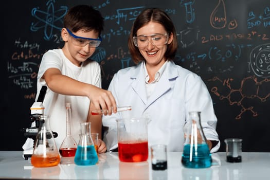 Teacher support schoolboy in laboratory. Schoolboy and teacher stand and experiment about science of chemistry in STEM class using liquid in glass container. Instructor mixing solution. Erudition.