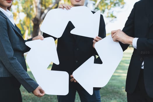 Business people holding pieces of reverse arrow icon into recycle symbol together in outdoor nature, promoting Earth cleaning day with zero waste pollution by embrace recycle reduce reuse idea. Gyre