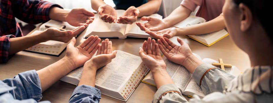 Cropped image of diversity people hand praying together at wooden church on bible book. Group of believer hold hand together faithfully. Concept of hope, religion, faith, god blessing. Burgeoning.