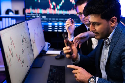 Two stock exchange traders researching data on smartphone and laptop screen server of dynamic digital currency. Investors analyzing market stock at decorative neon blue-light of workplace. Sellable.