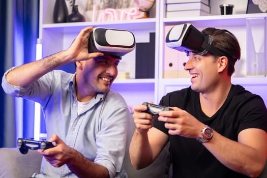 Buddy friend gamers playing video game using joysticks and VR headset of virtual technology in reality in studio room with neon blue light. Comfy living indoor with cheerful fighting winner. Sellable.