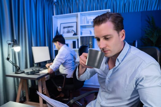 Business partner drinking cup of coffee, focusing on document sheet work at night time in modern office. Coworker analyzing on computer with creative project at blue neon decorative room. Sellable.