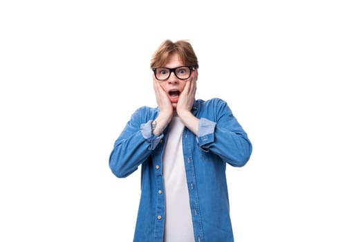 young surprised guy with red hair in a denim shirt on a white background with copy space.