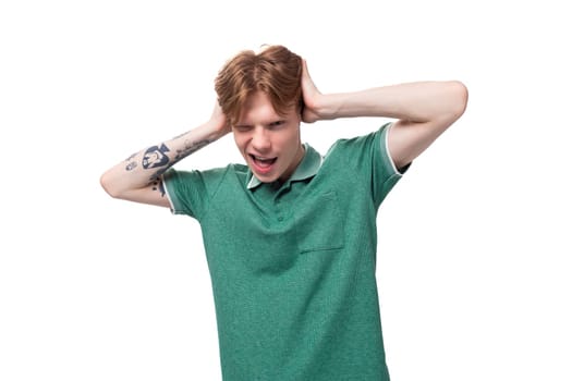 young charming adorable ginger man with a tattoo on his arm dressed in a green short sleeve t-shirt covers his ears with his hands.