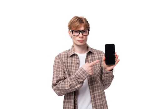 young man with red golden hair in glasses and a shirt holding a smartphone with a screen on an isolated background.