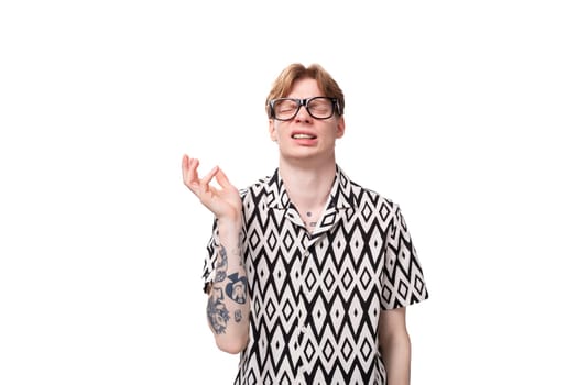 a young man with golden hair and a tattoo on his arms wears glasses for image and a black and white shirt.
