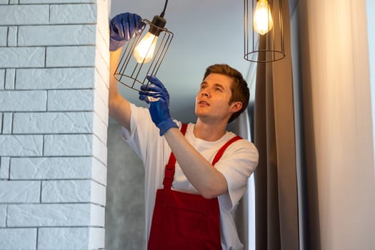 Electrician in uniform installing ceiling lamp indoors. Space for text.