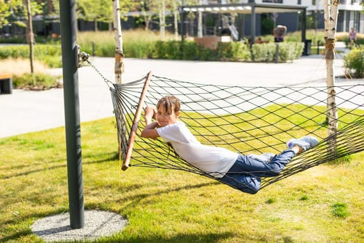 happy cheerful child smiling and lying, resting in a hammock in the woods in a glade in summer among the bright green grass. High quality photo