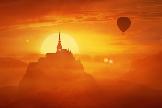 Beautiful sunset landscape over the misty kingdom between the orange hills in the center of nature and the silhouette of a flying air balloon. Fantasy world imaginary view, another reality concept.