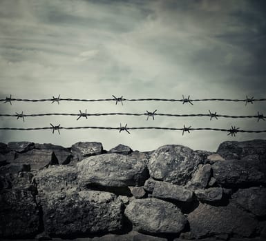 Masonry stone wall fence of a prison with barbed metallic wire above.