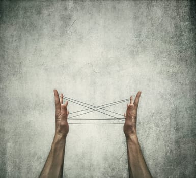 Two human hands playing cats cradle game with a thread on a grey concrete background. Creative thinking concept