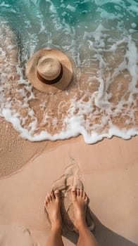 A person's feet on the beach with a hat and sand