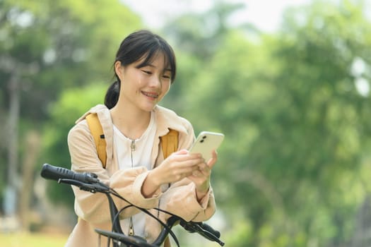 Attractive young woman standing near a bicycle at a city park and using a mobile phone.