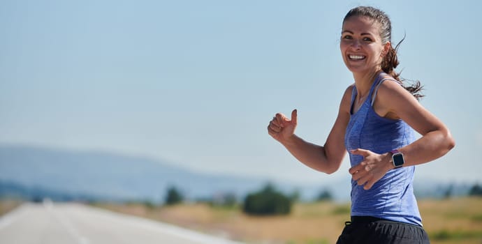 An athletic woman finds freedom and joy in a healthy lifestyle, running through a beautiful road trail at sunrise.