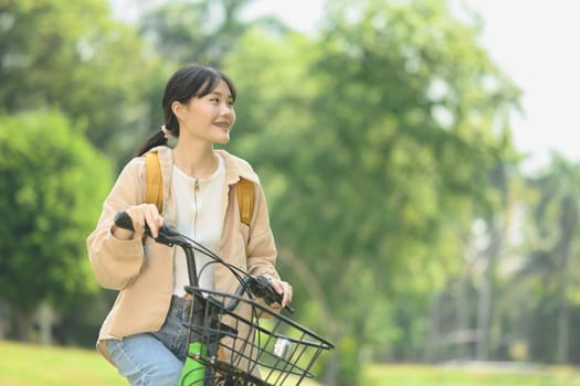 Positive young woman in casual clothes riding a bicycle in the park, enjoying nature. Active lifestyle concept.