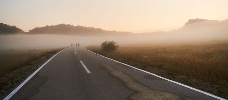 A group of friends, athletes, and joggers embrace the early morning hours as they run through the misty dawn, energized by the rising sun and surrounded by the tranquil beauty of nature.