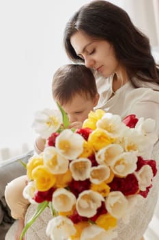 Cute little baby daughter and mom with flowers tulips. Mother and child hugging. Happy mother's day.