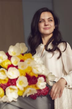 Beautiful woman with spring flowers tulips in hands sitting on chair near window. Women's Day