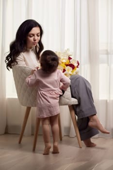 Cute little baby daughter and mom with flowers tulips. Mother and child hugging. Happy mother's day.