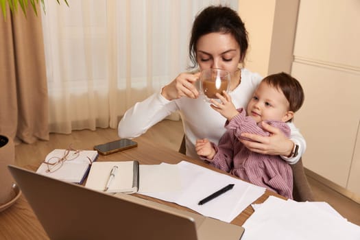 beautiful businesswoman working at home with her little child girl and drinking coffee