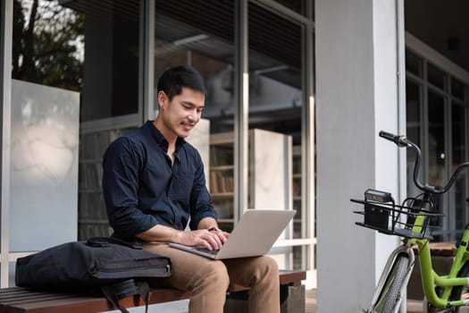 A young Asian businessman rides a bicycle to work. Use a reusable water bottle. Working outside of the office using a laptop The concept of saving energy and reducing pollution to the environment..