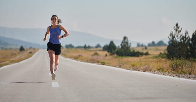 An athletic woman finds freedom and joy in a healthy lifestyle, running through a beautiful road trail at sunrise.