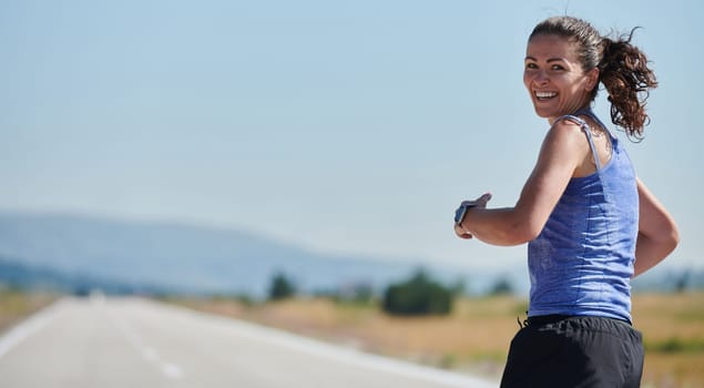 An athletic woman finds freedom and joy in a healthy lifestyle, running through a beautiful road trail at sunrise.