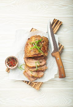 Rolled turkey roasted with spices and herbs on baking paper with knife and wooden white background top view. Baked cut for slices turkey fillet roll for dinner.