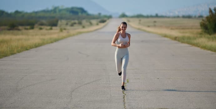 An athletic woman finds freedom and joy in a healthy lifestyle, running through a beautiful road trail at sunrise.