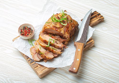 Rolled turkey roasted with spices and herbs on baking paper with knife and wooden white background top view. Baked cut for slices turkey fillet roll for dinner.