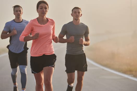 A group of friends, athletes, and joggers embrace the early morning hours as they run through the misty dawn, energized by the rising sun and surrounded by the tranquil beauty of nature.