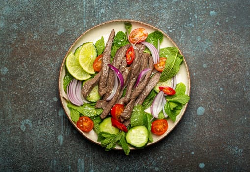 Plate with traditional Thai beef salad with vegetables and mint top view served on rustic concrete stone background, healthy exotic asian meal.