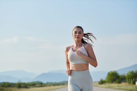 An athletic woman finds freedom and joy in a healthy lifestyle, running through a beautiful road trail at sunrise.