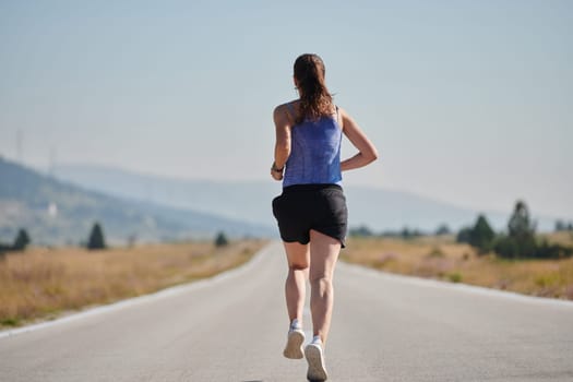 An athletic woman finds freedom and joy in a healthy lifestyle, running through a beautiful road trail at sunrise.