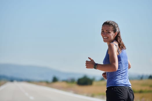 An athletic woman finds freedom and joy in a healthy lifestyle, running through a beautiful road trail at sunrise.