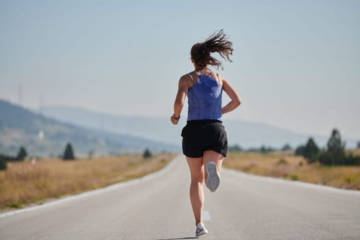 An athletic woman finds freedom and joy in a healthy lifestyle, running through a beautiful road trail at sunrise.