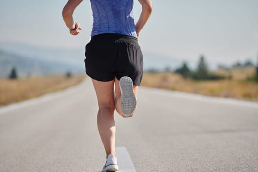 An athletic woman finds freedom and joy in a healthy lifestyle, running through a beautiful road trail at sunrise.