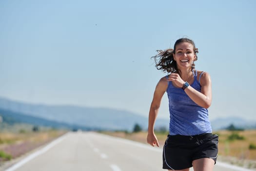 An athletic woman finds freedom and joy in a healthy lifestyle, running through a beautiful road trail at sunrise.