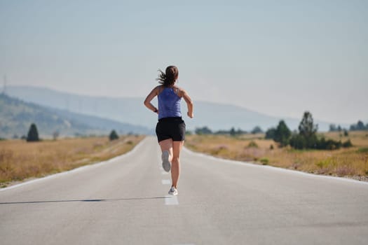 An athletic woman finds freedom and joy in a healthy lifestyle, running through a beautiful road trail at sunrise.